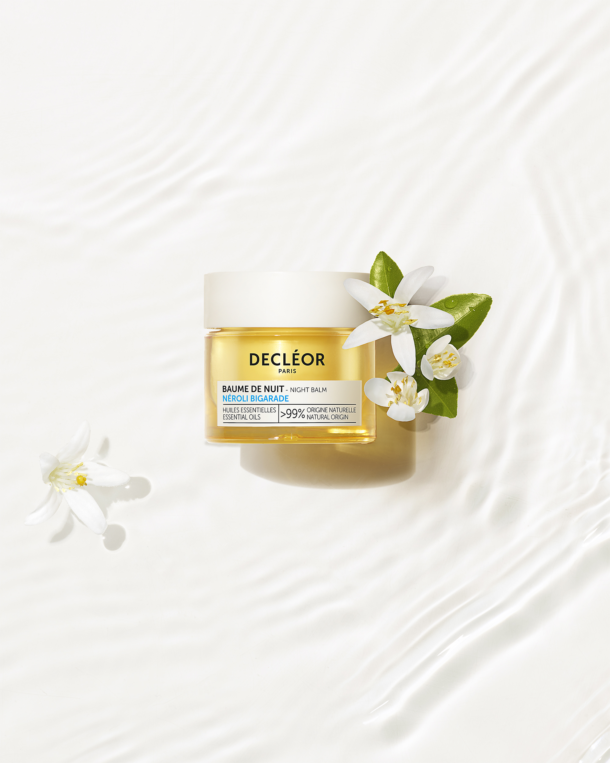 baume de nuit Decléor dans l'eau claire avec des fleurs blanches